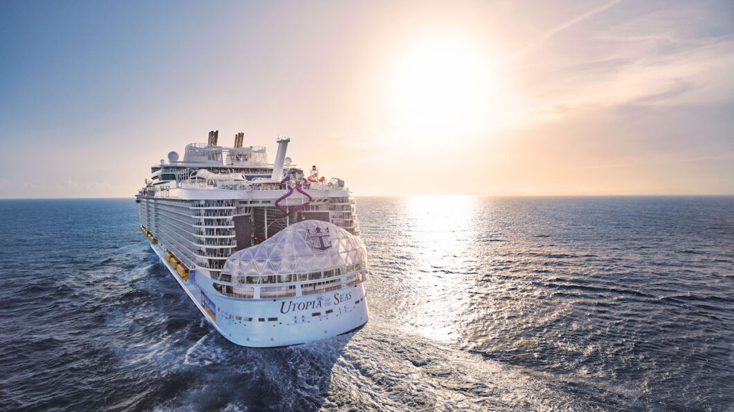 default A large cruise ship sails on the ocean under a clear sky with the sun setting on the horizon.