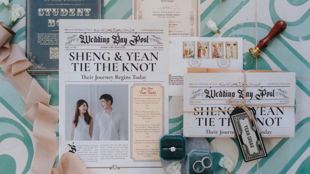What to Do When Someone Invites Themselves to Your Destination Wedding A wedding invitation suite themed as newspapers, featuring the couple Sheng and Yean, wedding details, rings in boxes, and various decorative elements on a patterned surface.